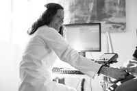 Frau Marika Ciba misst im wei&szlig;en Arztkittel am Elektromyographie (EMG) Werte eines Patienten